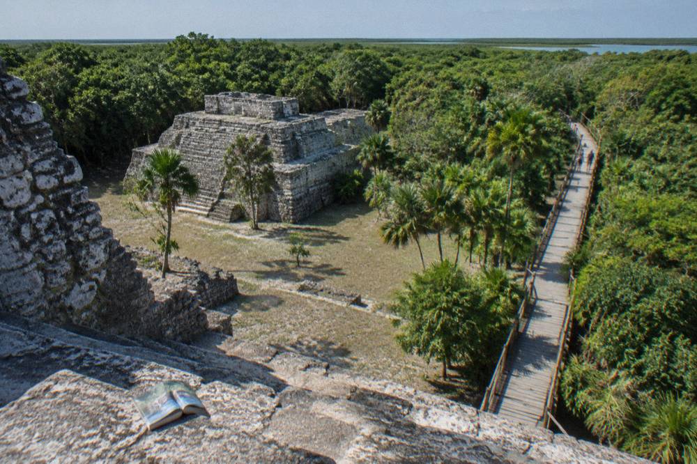 Ancient stone ruins of Muyil beside a wooden walkway leading toward green jungle