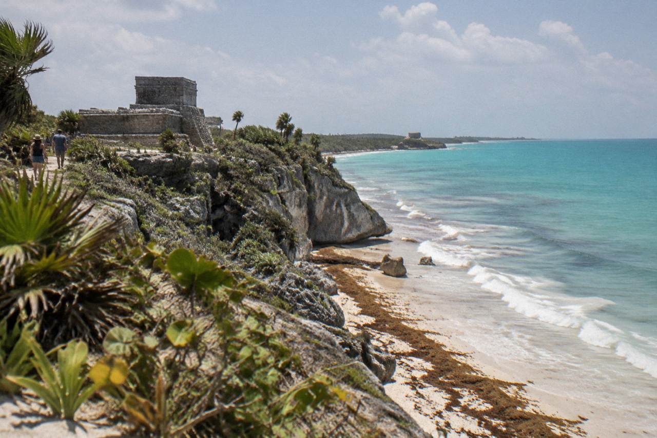 Stone Maya structure standing above low jungle canopy near a lagoon